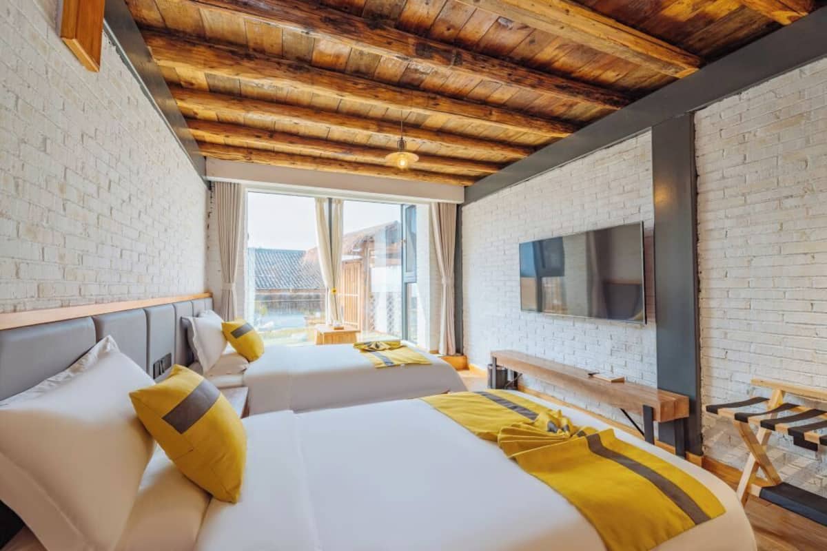 A hotel room with two beds, a TV, and a wooden ceiling.