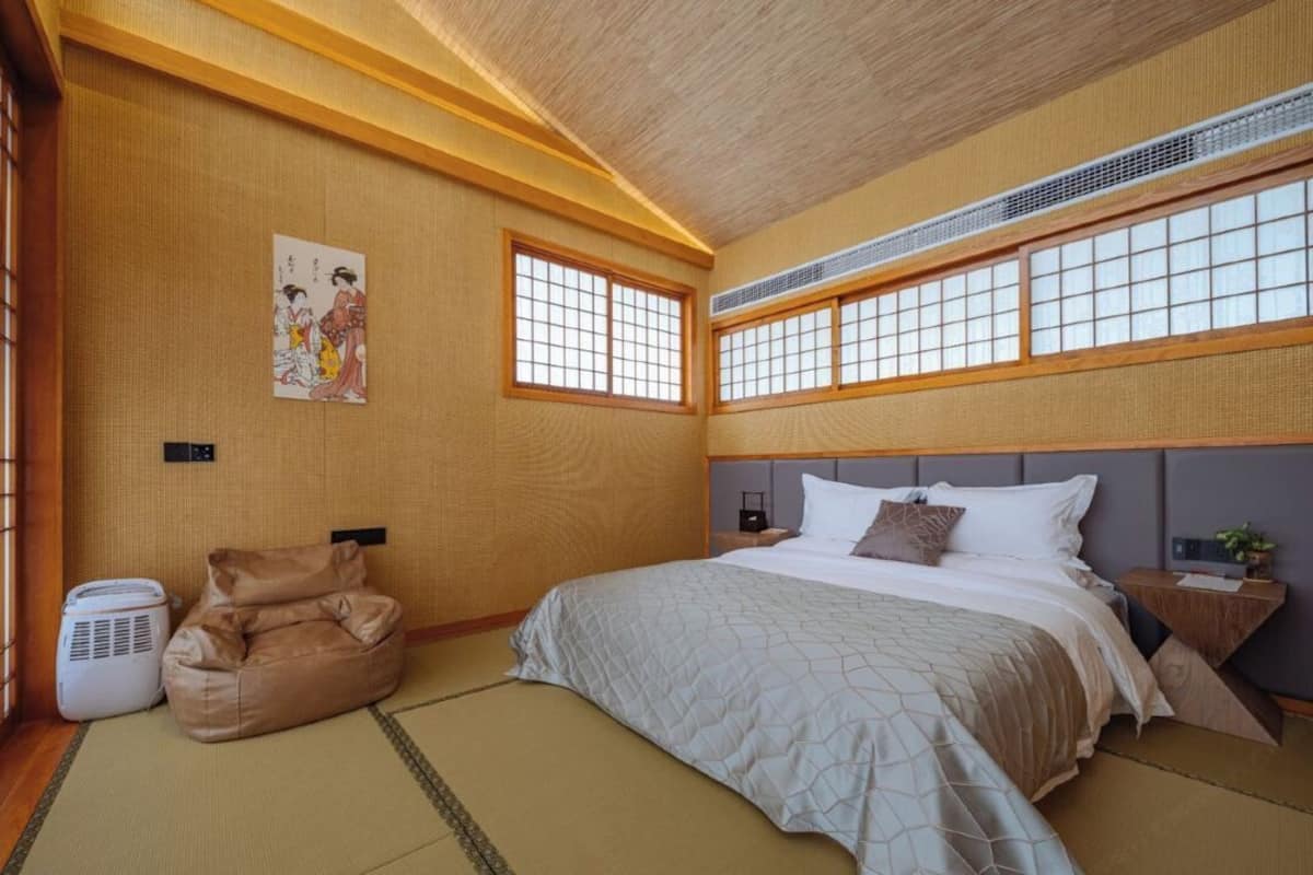 A traditional Japanese-style bedroom with tatami flooring, a bed with a headboard, a futon, and a shoji screen window.