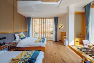 Habitación de hotel con dos camas, un escritorio, una silla, una mesita y un ventanal con cortinas.