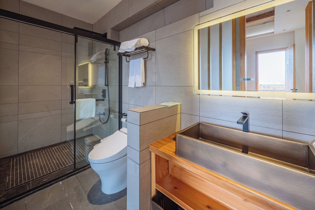 Un baño moderno con cabina de ducha de vidrio, inodoro, tocador de madera y un espejo grande.