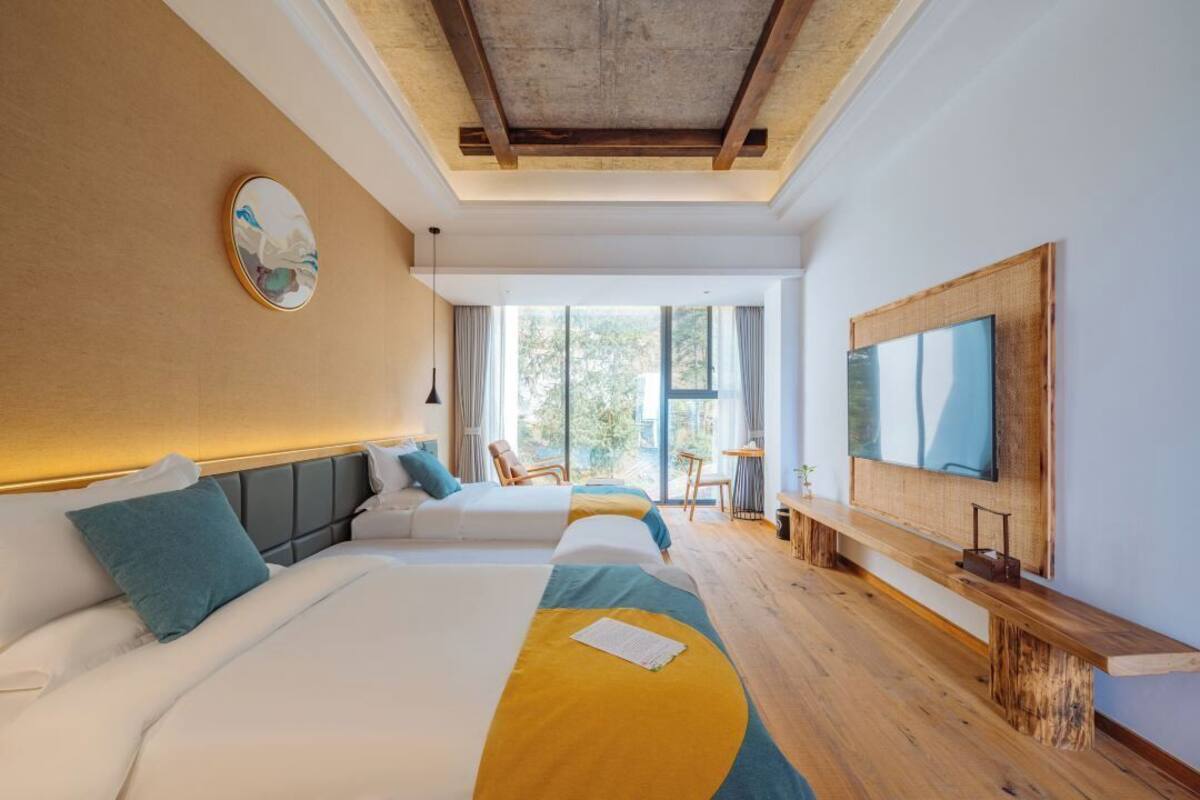 A modern hotel room with two beds, a large TV, and a view of the outdoors.