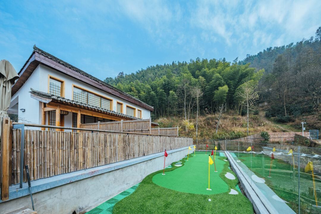 A traditional-style building with a wooden fence and a green artificial turf area with golf-like markers.