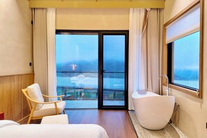 A hotel room with a large bathtub, a chair, a bed, and a balcony with a view. - Yichun Old Yu Xinzhi Homestay (Yichun)