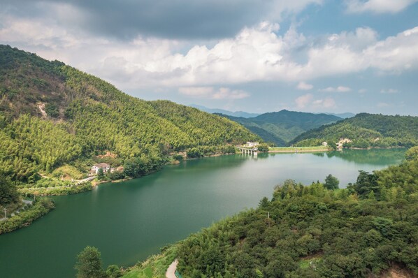 A serene lake surrounded by lush green hills, a bridge, and a few buildings.