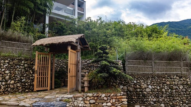 A traditional wooden gate leading to a stone wall, surrounded by lush greenery and a mountain backdrop. - Yichun Old Yu Xinzhi Homestay (Yichun)