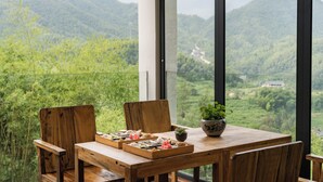 A wooden dining table with chairs and a potted plant, set against a backdrop of lush green mountains and a clear sky. - Yichun Old Yu Xinzhi Homestay (Yichun)