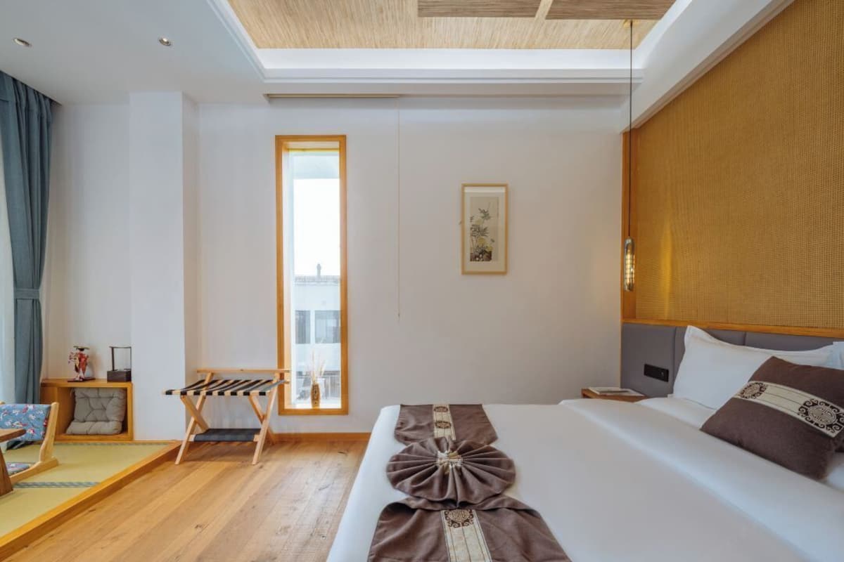 A modern hotel room with a large bed, a wooden ceiling, a window, and a small seating area.