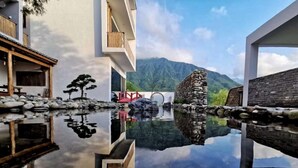 A modern building with a reflective pool, a traditional stone bridge, and a mountainous backdrop. - Yichun Old Yu Xinzhi Homestay (Yichun)