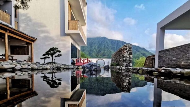 A modern building with a reflective pool, a traditional stone bridge, and a mountainous backdrop. - Yichun Old Yu Xinzhi Homestay (Yichun)