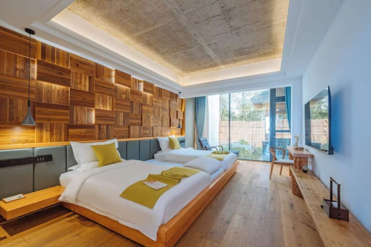 A modern bedroom with a wooden wall panel, two beds, a desk, and a TV.