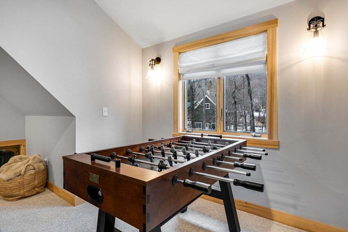 A foosball table in a room with a sloped ceiling, a window with a view of trees, and a bean bag chair.