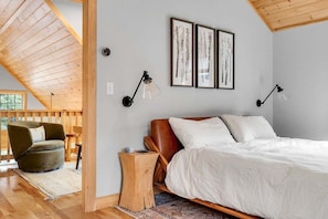 A bedroom with a sloped ceiling, a bed with white bedding, two wall-mounted lamps, and framed artwork. - Slopeside Chalet | Hot Tub| Sauna| Game Room (Newry)