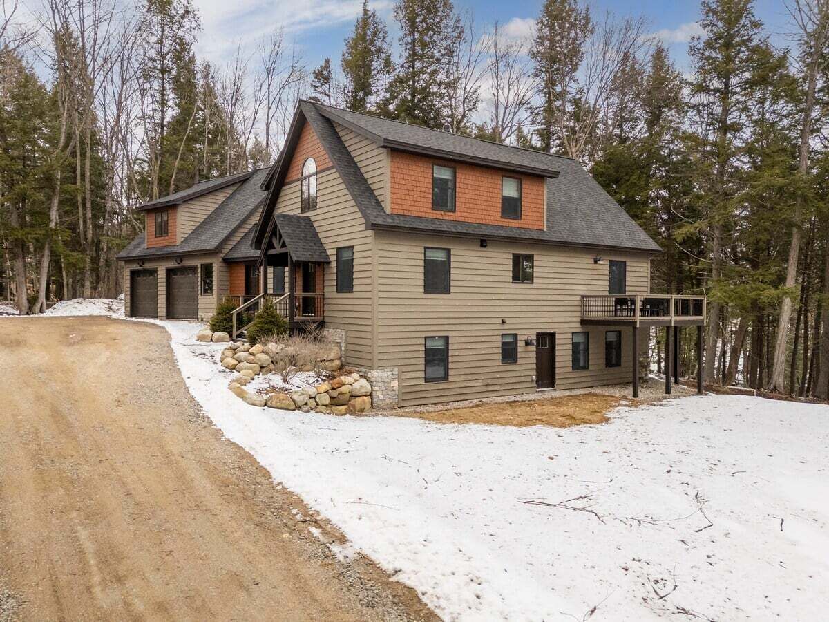 A two-story house with a sloped roof, a front porch, and a stone foundation.