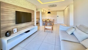 Un saló modern amb televisió plana, un sofà, zona de menjador amb cadires i una porta blanca.
