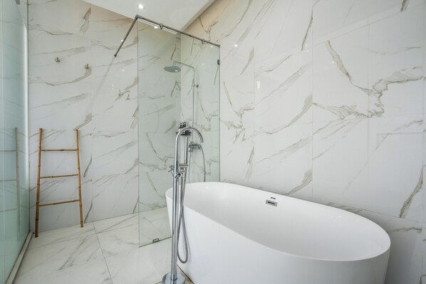 Une salle de bain moderne avec une baignoire sur pieds, une douche à parois de verre et des murs en marbre.