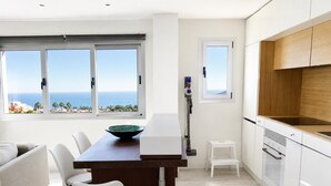 Une cuisine moderne avec vue sur la mer, un coin repas avec un canapé blanc et un petit tabouret blanc.