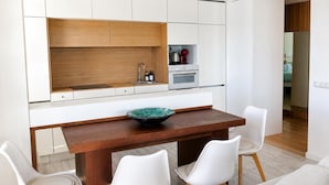 Une cuisine moderne avec des meubles blancs, un plan de travail en bois, un évier et une cuisinière. On y trouve deux chaises blanches et un saladier posé sur le plan de travail.