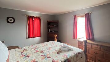A bedroom with a bed, a dresser, a clock, and a window with curtains.