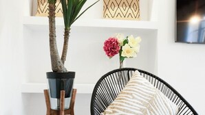Ein Wohnzimmer mit Blumentopf, einem Sessel mit gemustertem Kissen und einer Vase mit Blumen.