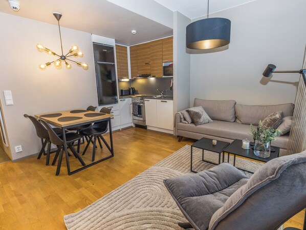 A modern living space with a dining area, a sofa, and a kitchen.