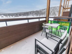 A balcony with a view of a snowy forest. There is a table with chairs and a small house model.