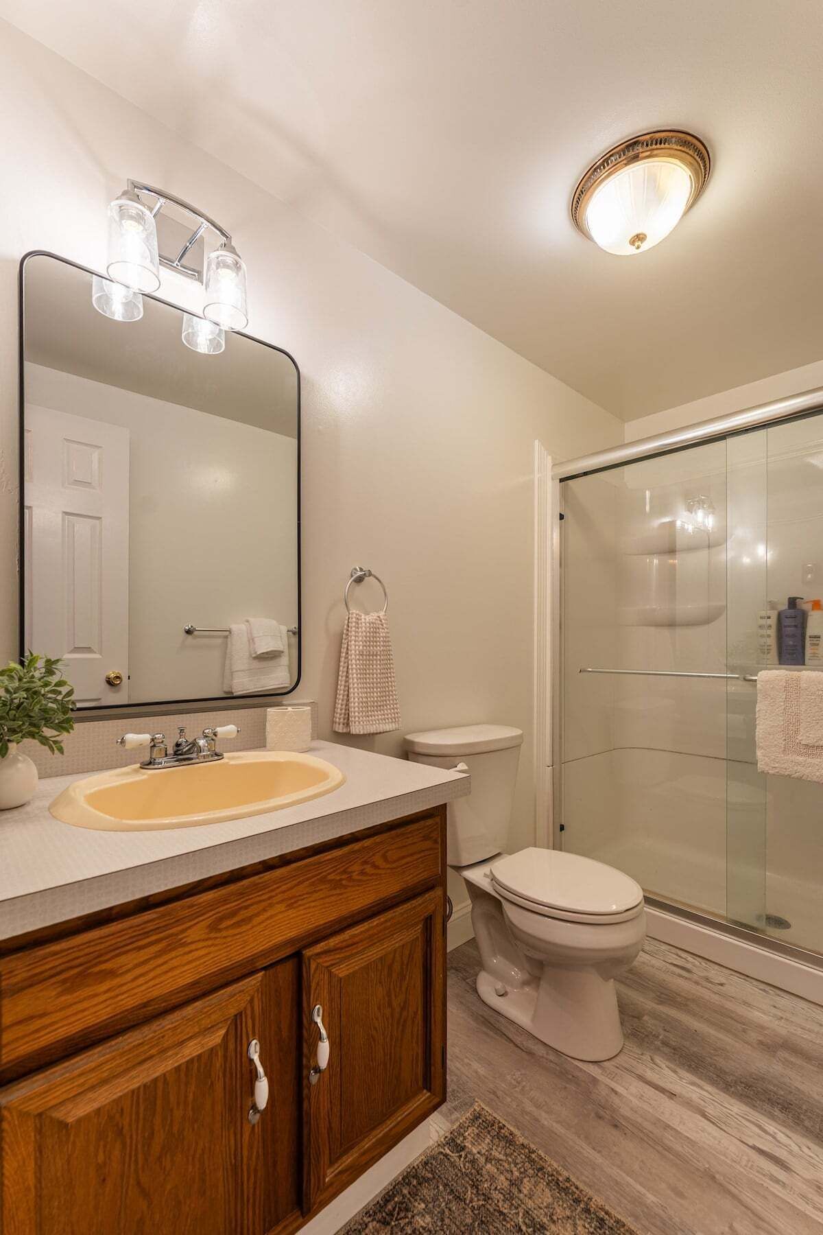 A bathroom with a wooden vanity, a large mirror, a toilet, and a glass shower enclosure.