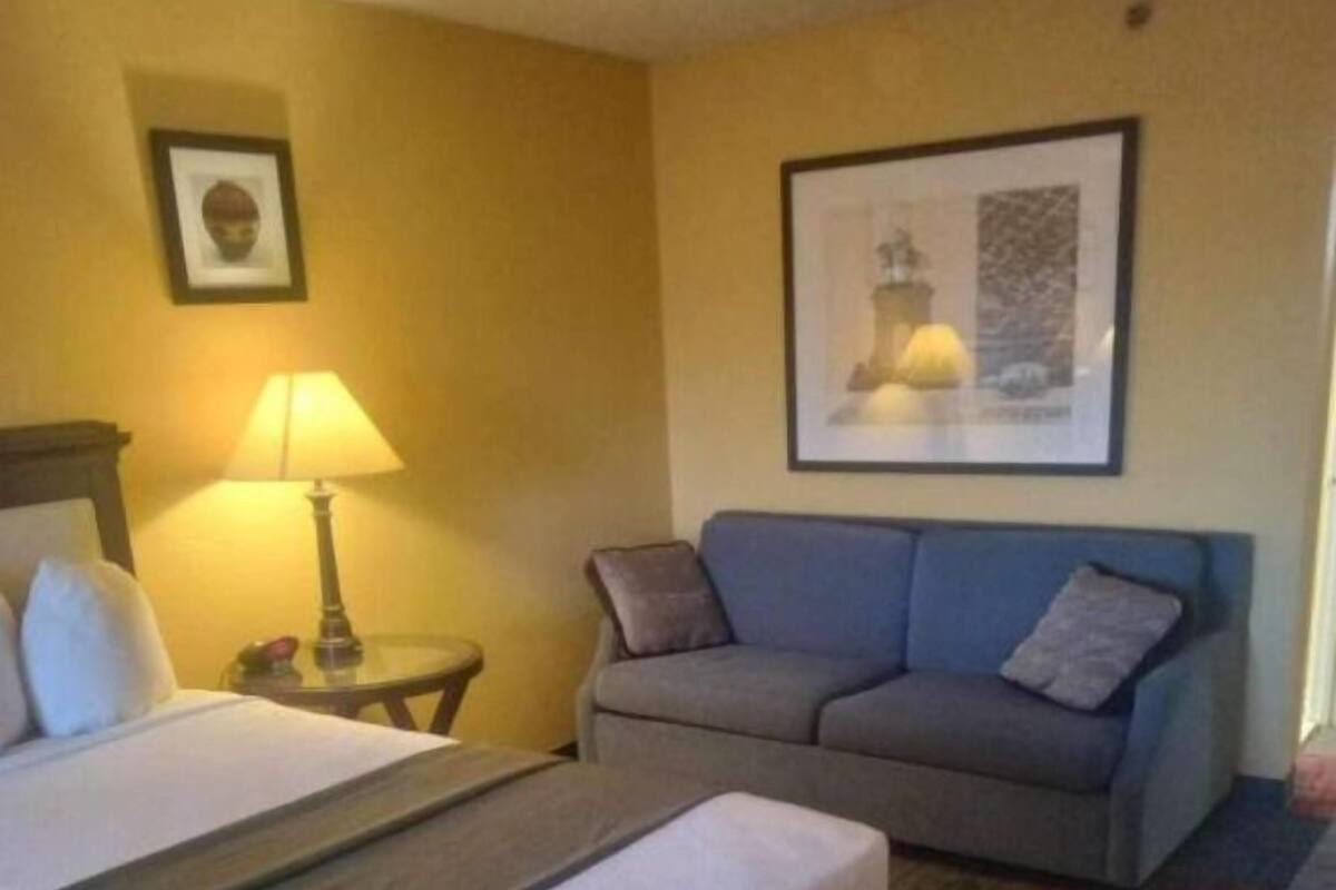 A hotel room with a bed, a sofa, a lamp, and two framed pictures on the wall.