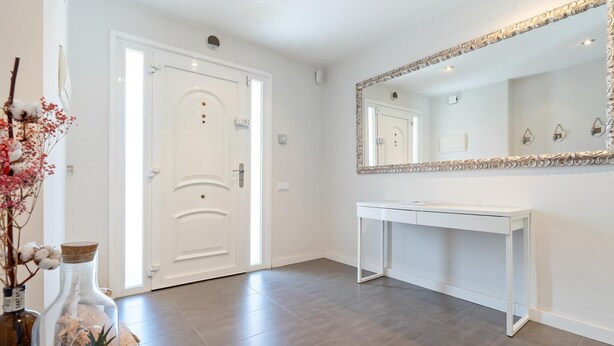 Un couloir propre et moderne, avec une porte blanche, un grand miroir et une console blanche.