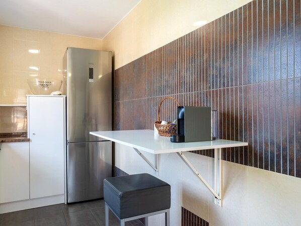 A modern kitchen with a stainless steel refrigerator, a white countertop, and a wall-mounted shelf with a basket and a coffee maker.