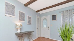 A hallway with a wooden floor, a white door with a glass panel, and a wall with framed abstract art. - The Largo Coastal Cottage (Largo)
