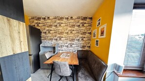 Une cuisine compacte avec un mur en pierres apparentes derrière l’évier, une table à manger avec des chaises et un banc intégré.