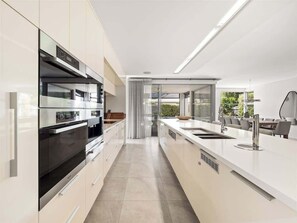 A modern kitchen with stainless steel appliances, a large island with a sink, and a view of the outdoors. - Peppermint Paradise—Seaside Comfort & Home Theatre (Dunsborough)