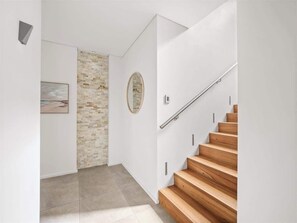 A modern interior with a wooden staircase, a stone wall, and a framed picture.
