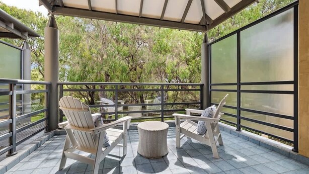 Un espacio de estar cubierto al aire libre con dos sillas Adirondack y una mesa redonda, con vistas a un jardín.