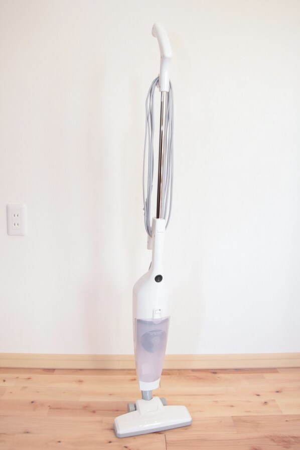 A white upright vacuum cleaner on a wooden floor with a plain white wall in the background. - BATH (Beppu)