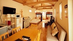 A room with wooden ceiling beams, bunk beds, a dining table with chairs, a sofa, a TV, and a kitchen area with appliances. - BATH (Beppu)