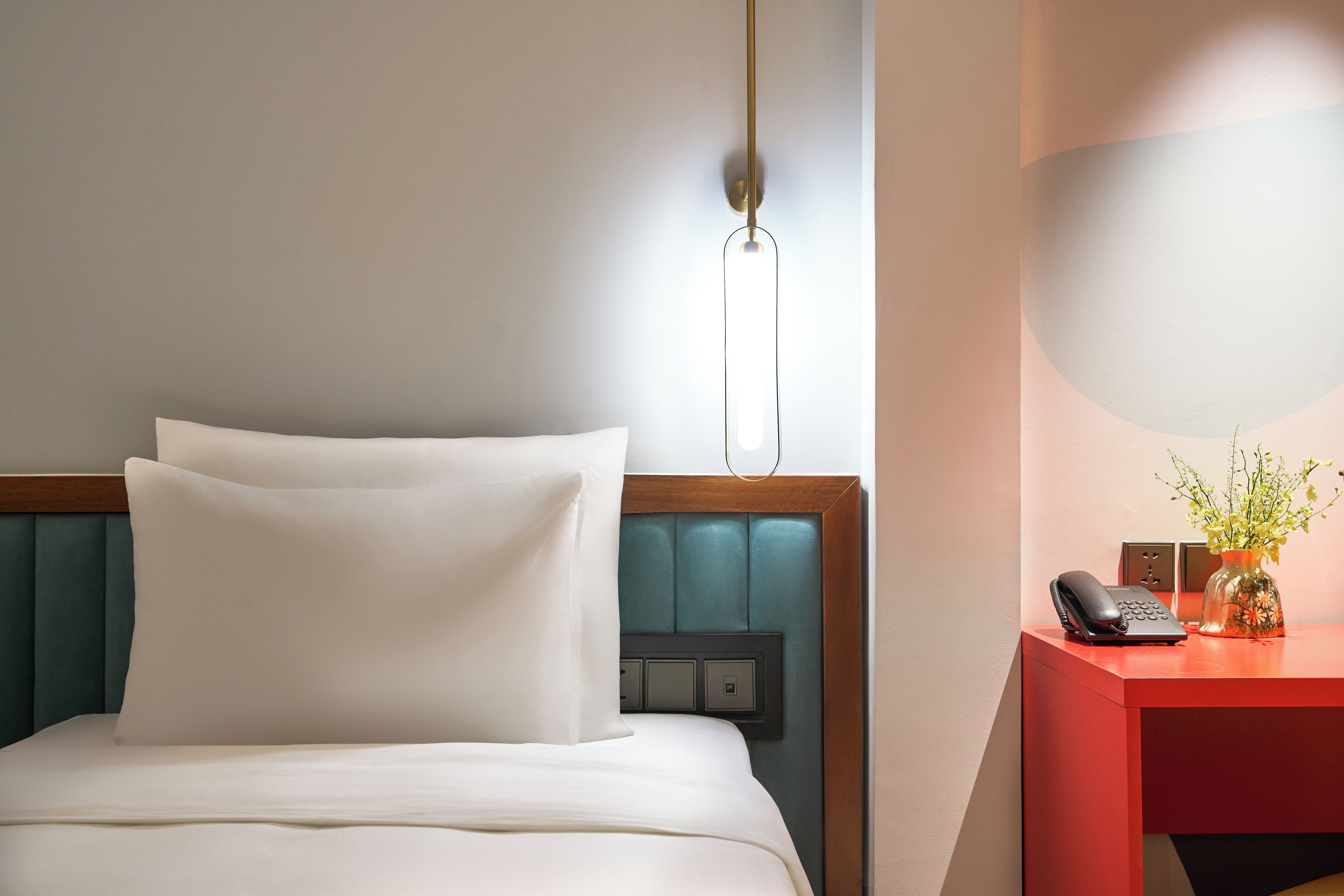 A hotel room with a bed, a desk with a telephone, and a vase with flowers.