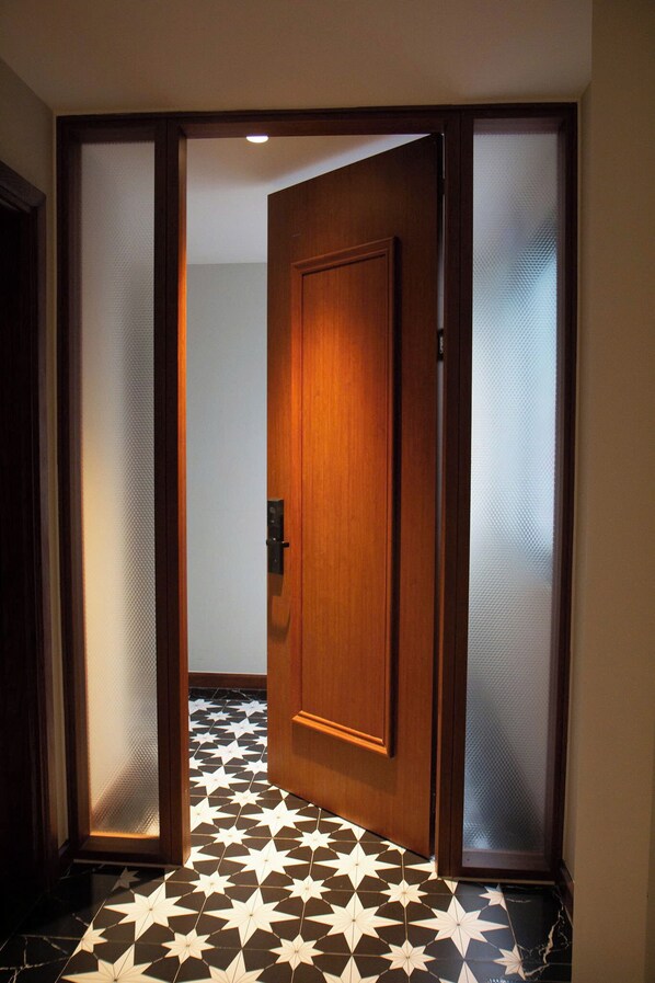 Une porte en bois avec un panneau en verre dépoli, qui donne sur une pièce dont le sol est recouvert d’un motif à étoiles en noir et blanc.
