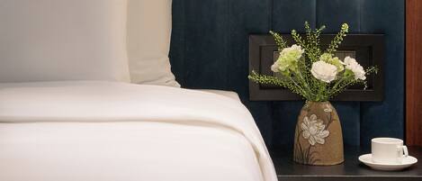 Una habitación de hotel con cama, mesita de noche, un florero con flores y una taza.