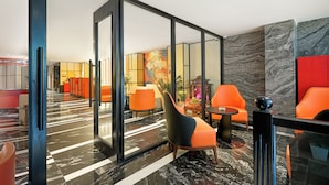 A modern lobby with a glass partition, orange seating, and a marble floor. - Solaria Tesori Hotel (Hanoi)