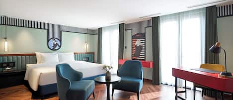 A hotel room with a bed, two armchairs, a desk, and a small table with a vase.