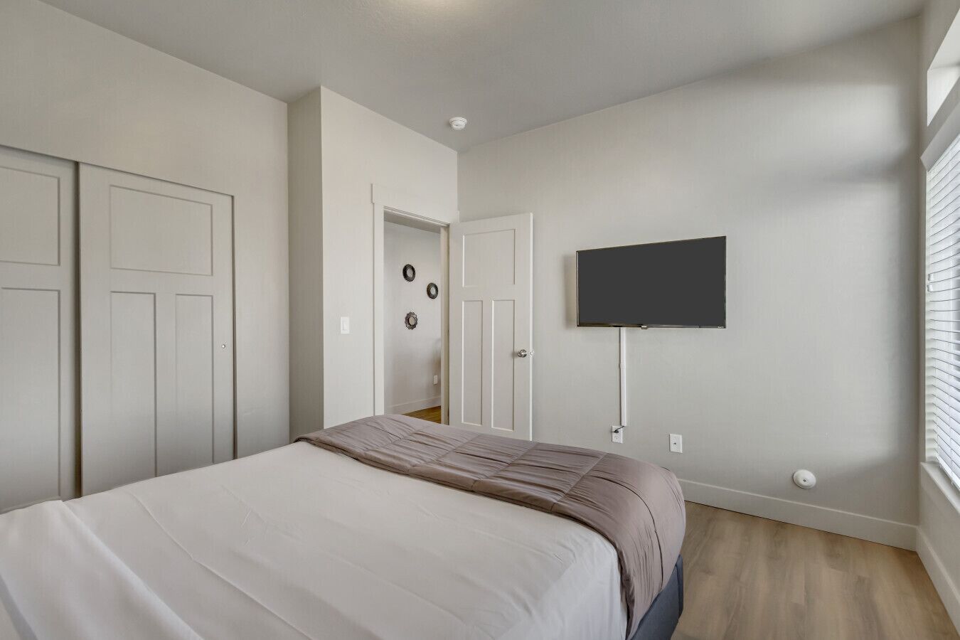 A bedroom with a bed, a TV mounted on the wall, and a door leading to another room.