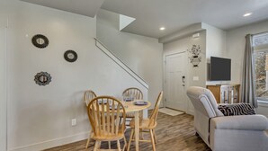 A modern living room with a sofa, a dining area with wooden chairs and a table, a staircase, and a TV on a stand. - Convenient 3BR with King Beds Near Hill AFB and Davis Conference Center (Layton)