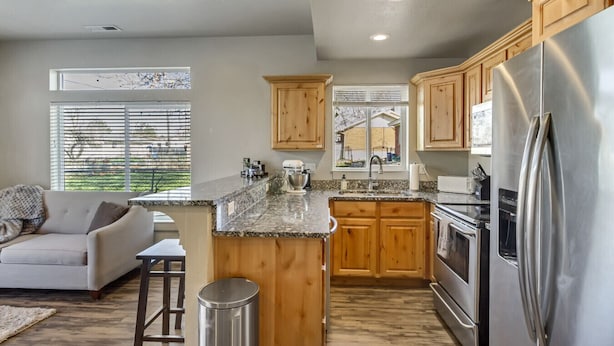 A modern kitchen with wooden cabinets, a stainless steel refrigerator, and a granite countertop. - Convenient 3BR with King Beds Near Hill AFB and Davis Conference Center (Layton)