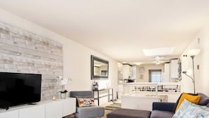 A modern living room with a flat-screen TV, a white console, a grey sofa, and a dining area with a white table and chairs. - Capitola Sands (Capitola)