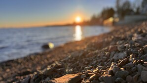 A pebble beach with the sun setting over the water. - Gooseberry Trailside Suites | Encampment River Suite (Two Harbors)