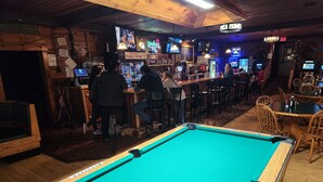 Una taula de bitlles en un bar amb parets de fusta i una zona de bar amb diverses pantalles i un cartell de neó.