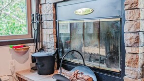 A stone fireplace with a 'Please Open Flue' sign, a pot on the mantel, a bowl with tools, and a log in a pan. - Gooseberry Trailside Suites | Lester River Suite (Two Harbors)