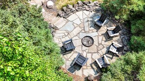 A circular stone patio with four Adirondack chairs and a central fire pit. - Gooseberry Trailside Suites | Lester River Suite (Two Harbors)
