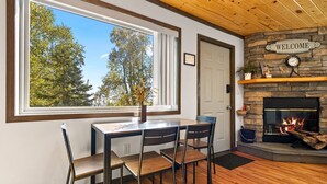 Una habitación acogedora con una mesa y sillas de madera, una chimenea y un gran ventanal con vistas a árboles.